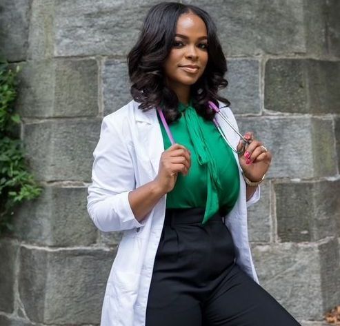 A woman in a white coat and green shirt is holding a stethoscope.