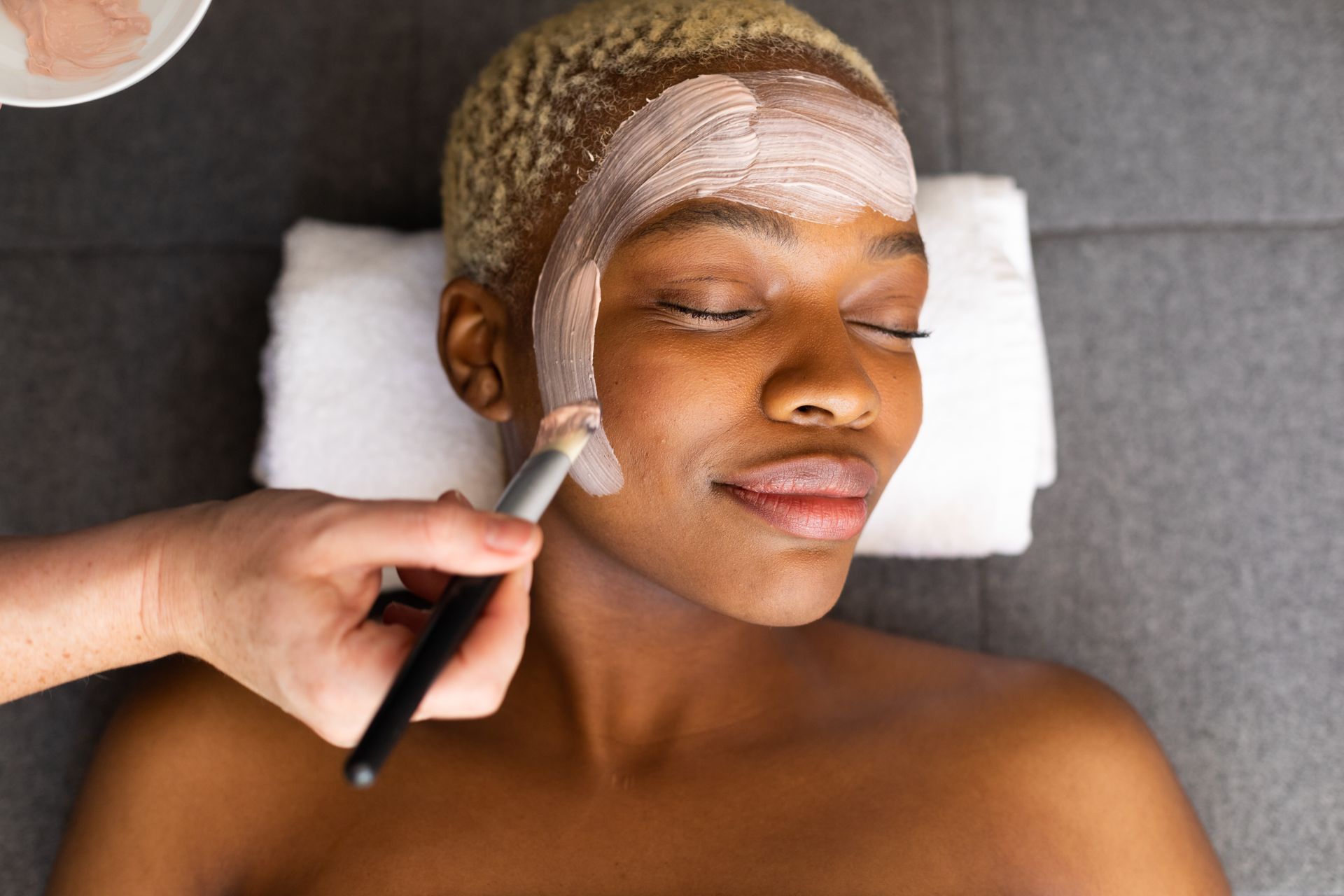Person receiving facial mask treatment at spa, applying pink clay mask.