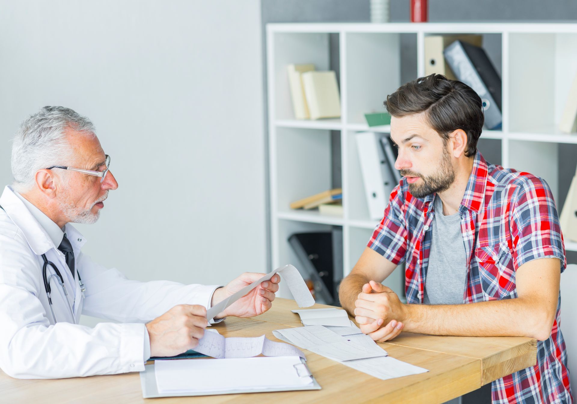 Doctor in lab coat showing a chart to a concerned patient in a plaid shirt.