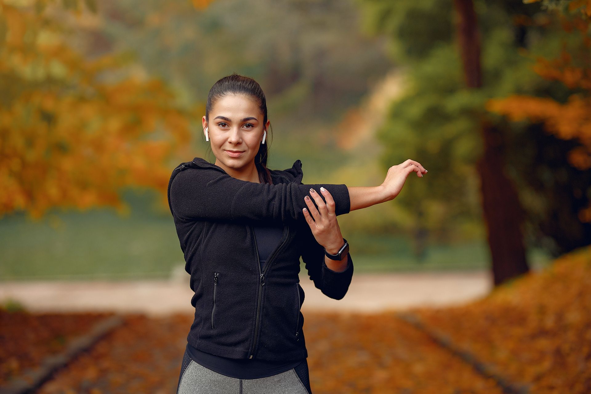 A woman is stretching her arms in a park.