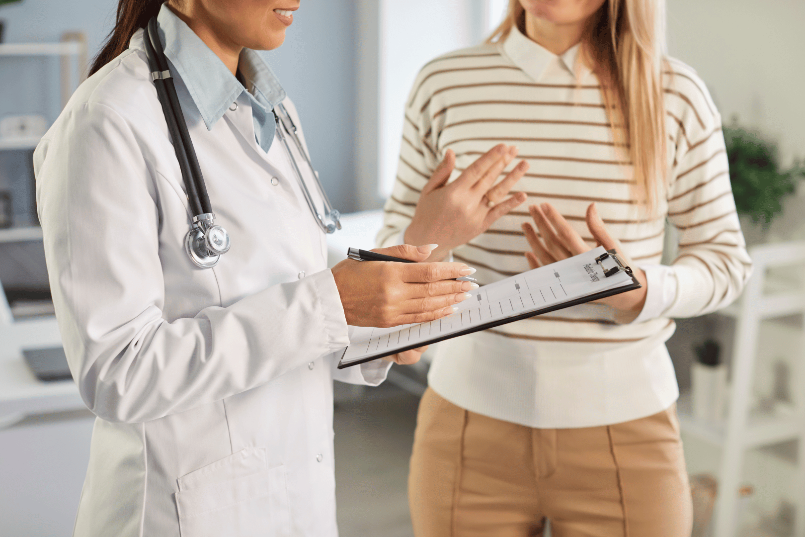 Doctor in lab coat and stethoscope with a patient, holding a clipboard and discussing.