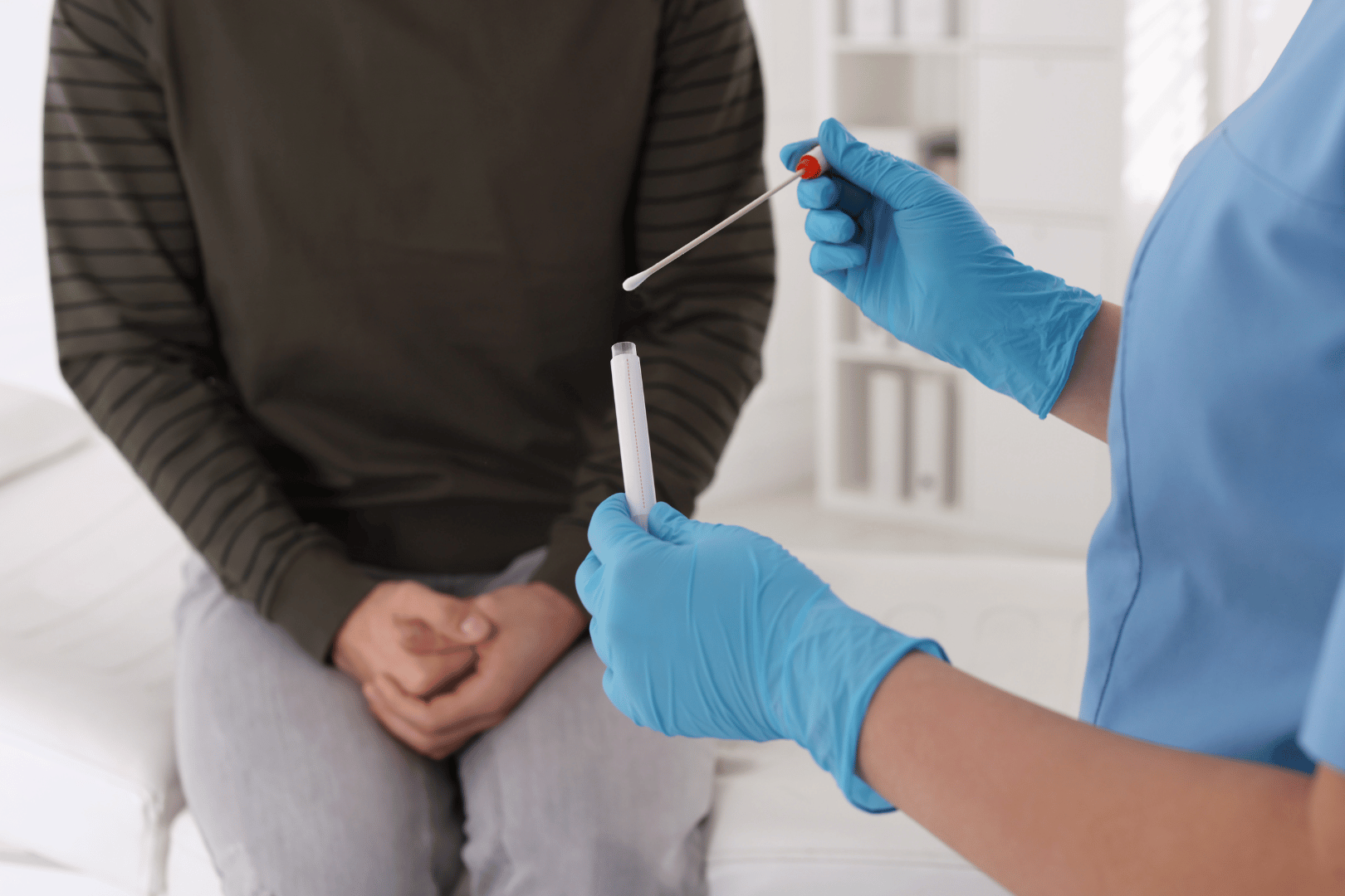 Healthcare worker with gloves preparing a swab test on a seated person.