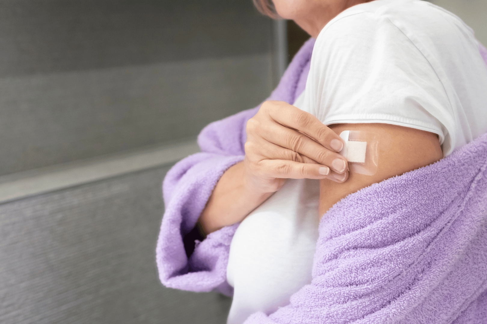 Person in robe applying a bandage to their upper arm, near a bathroom.