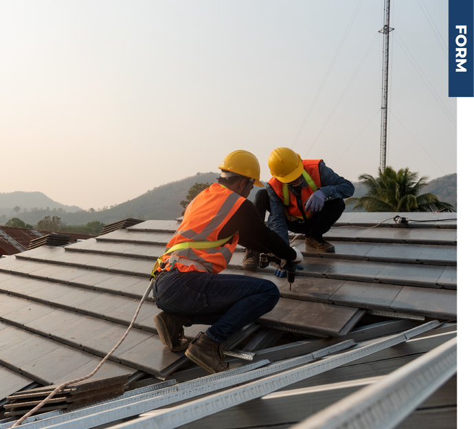 Two construction workers are working on the roof of a building.