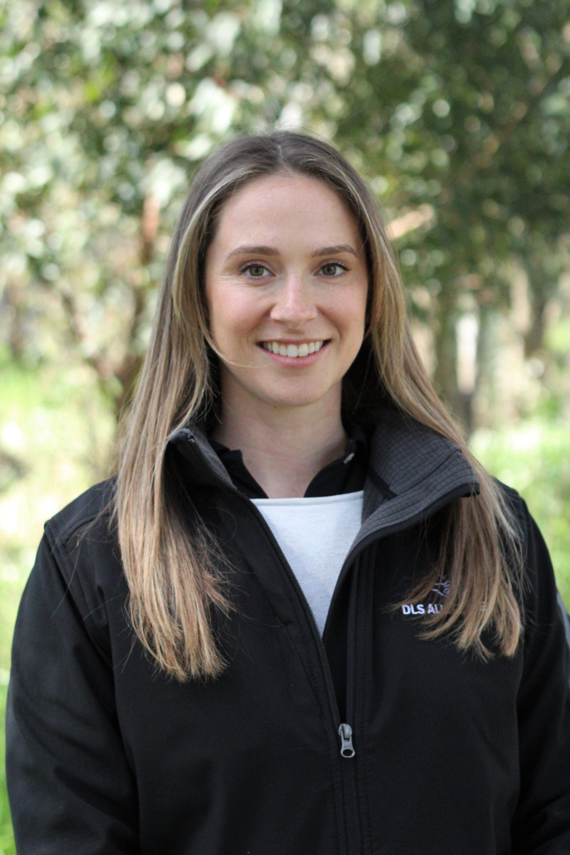 A woman wearing a black jacket and a white shirt is smiling for the camera.