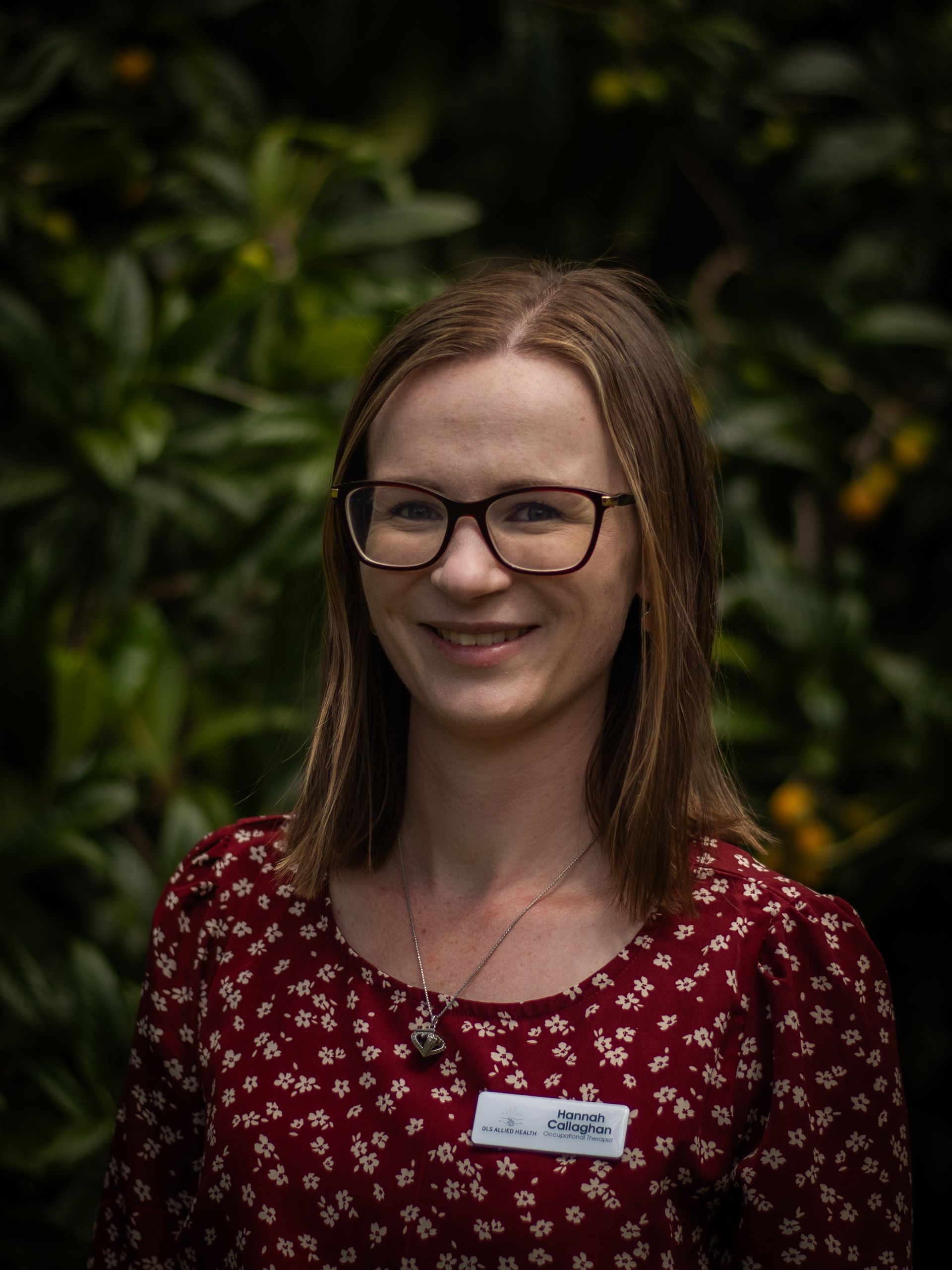 A woman wearing glasses and a name tag is smiling for the camera.