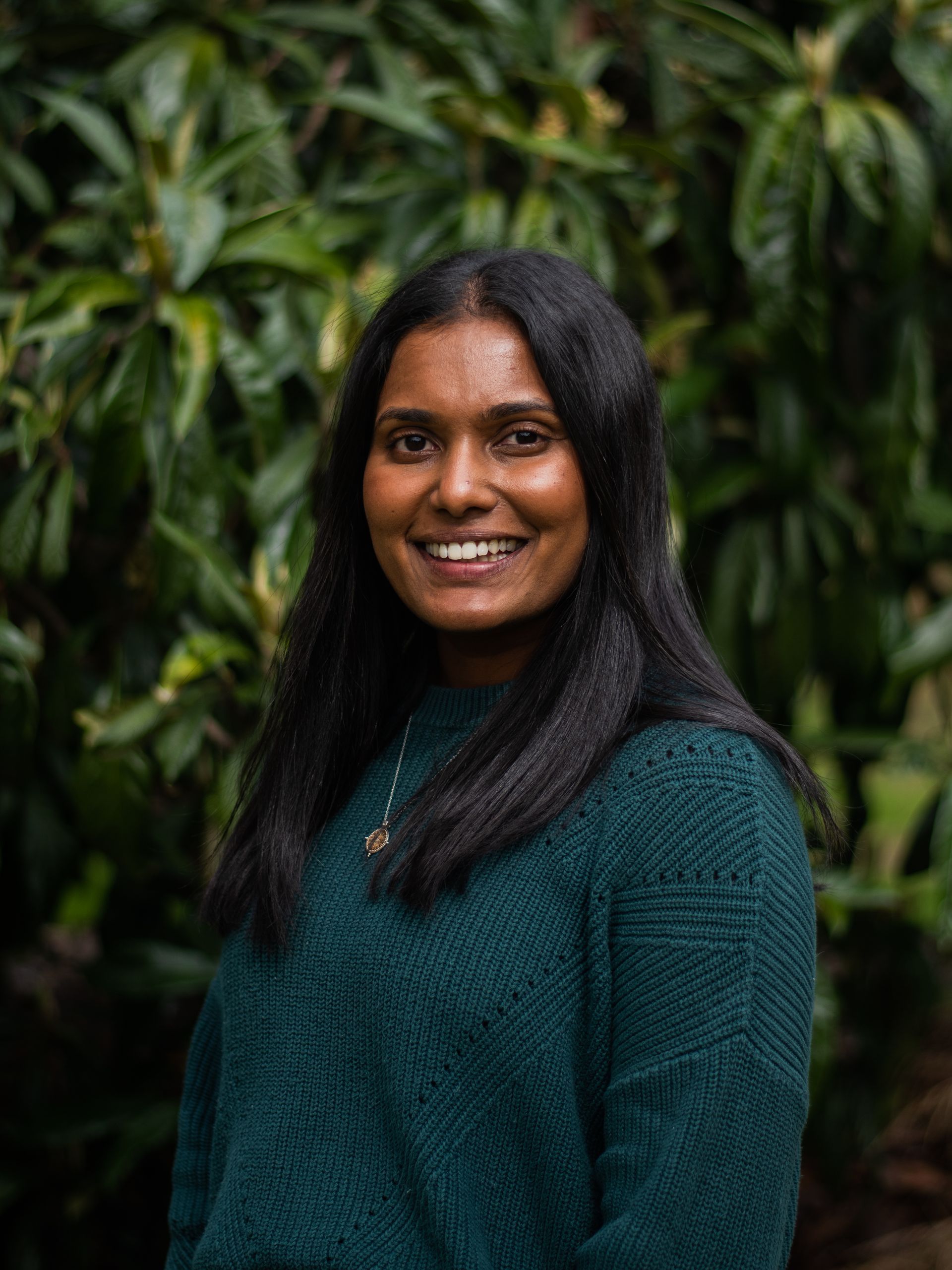 A woman in a green sweater is smiling in front of a tree.