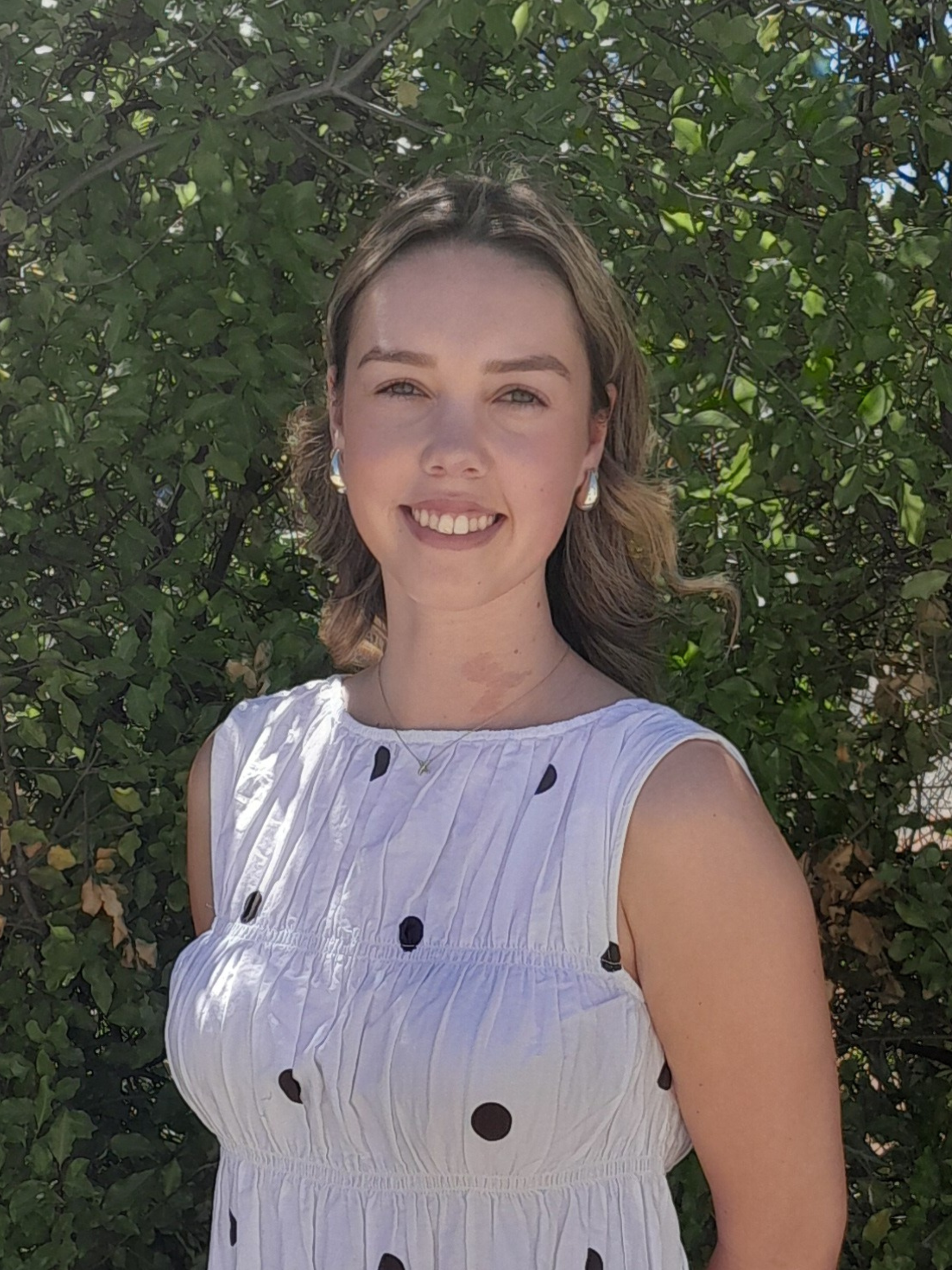 A woman in a black polka dot dress is standing next to a tree.