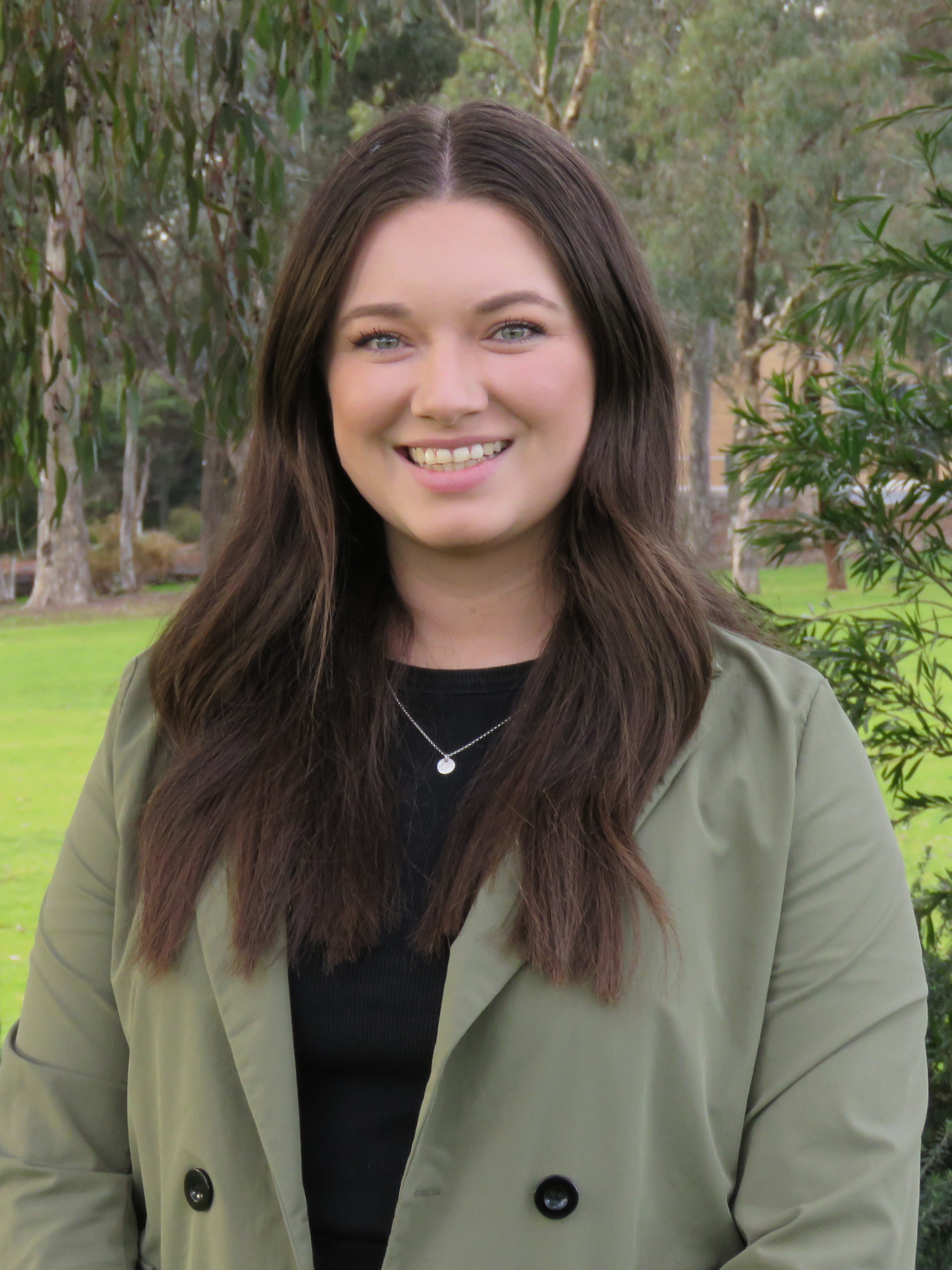 A woman in a green coat and black shirt is smiling for the camera.