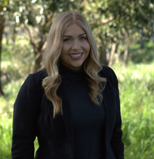 A woman in a black jacket is smiling for the camera while standing in a field.