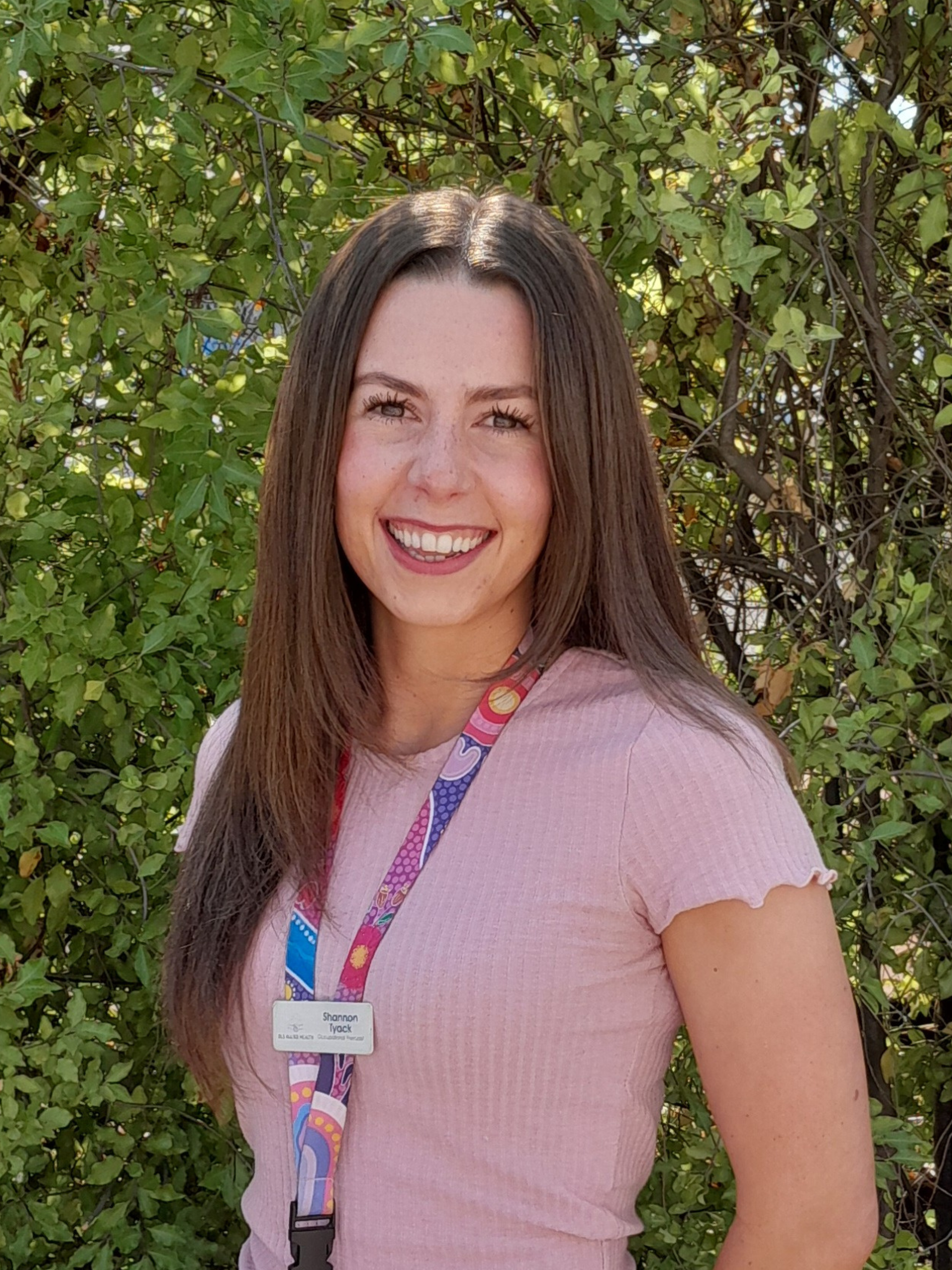 A woman in a black sweater with white polka dots is smiling in front of a bush.