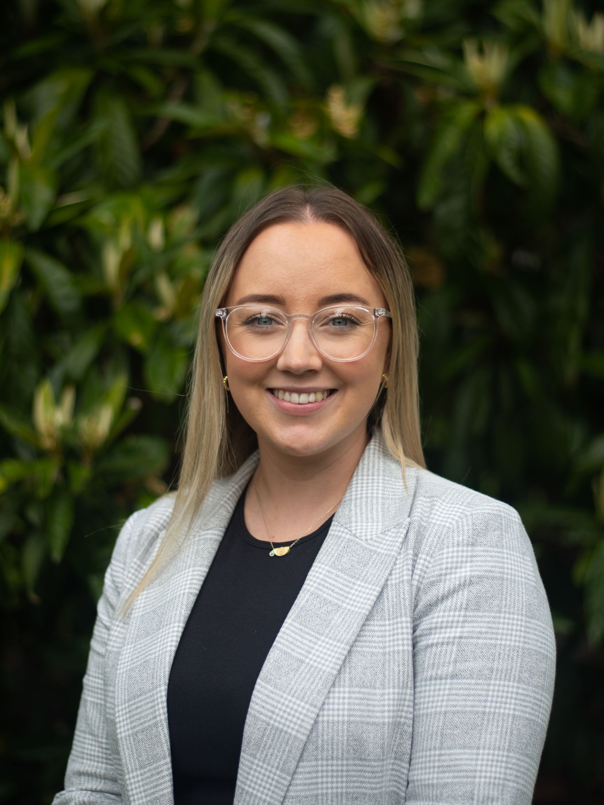 A woman wearing glasses and a grey jacket is smiling for the camera.