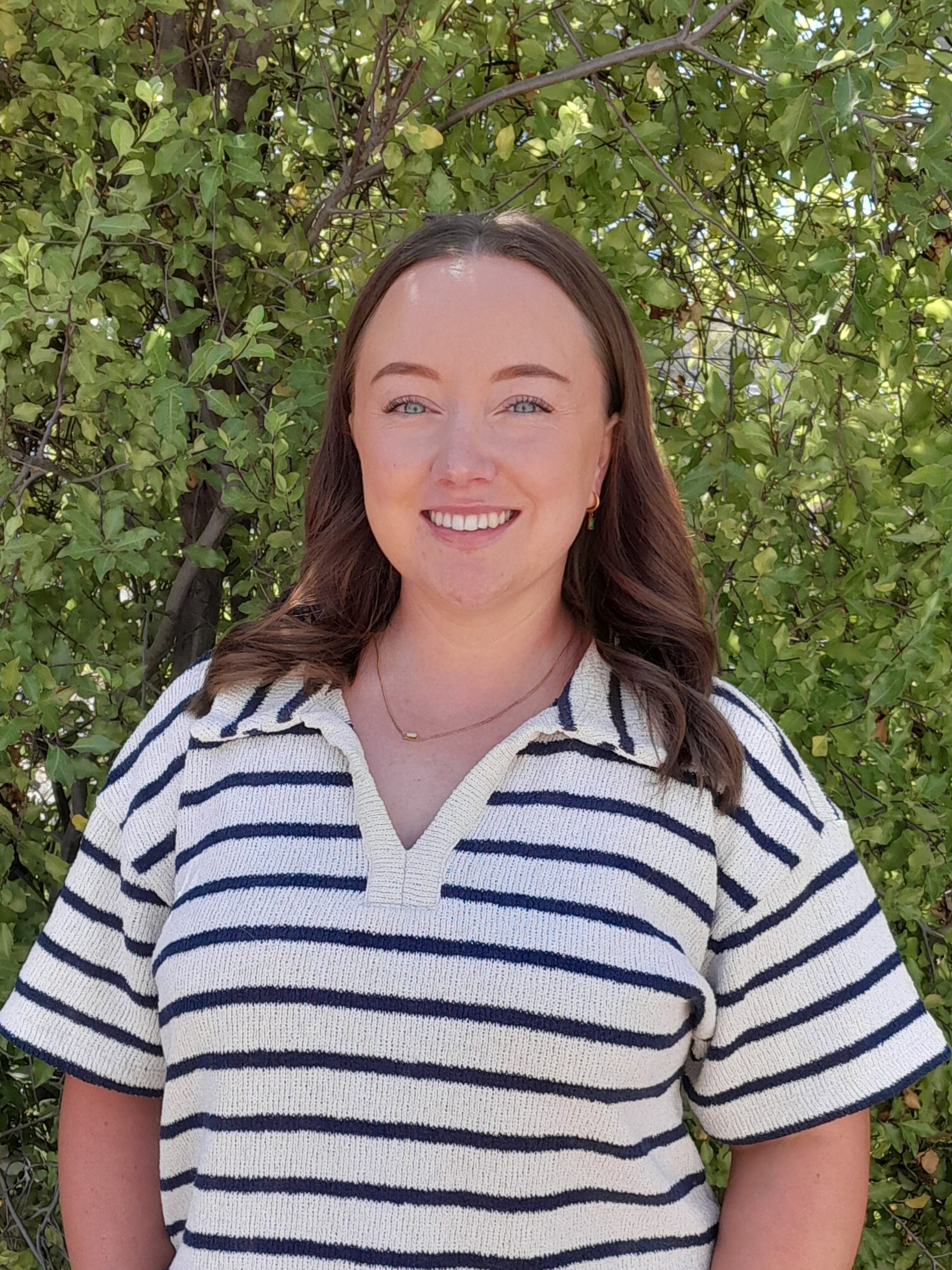 A woman wearing glasses and a grey jacket is smiling for the camera.