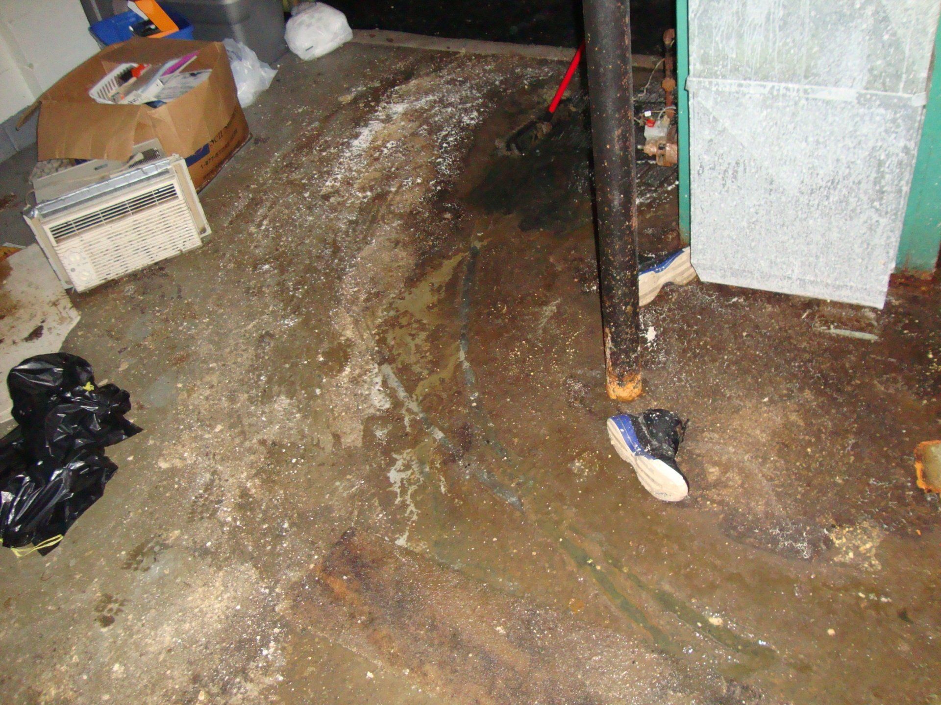 A person is standing on a dirty floor next to a pipe.