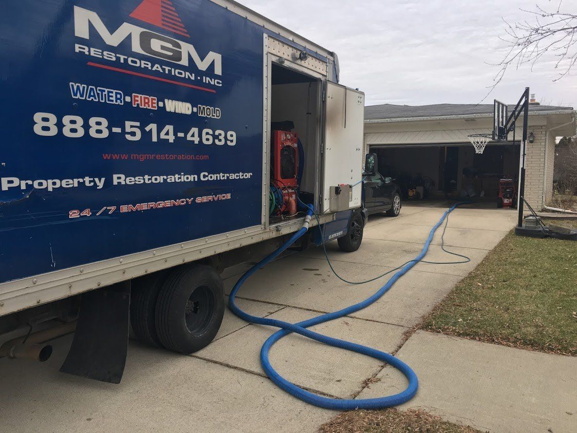 A blue and white m & m restoration truck is parked in front of a house.