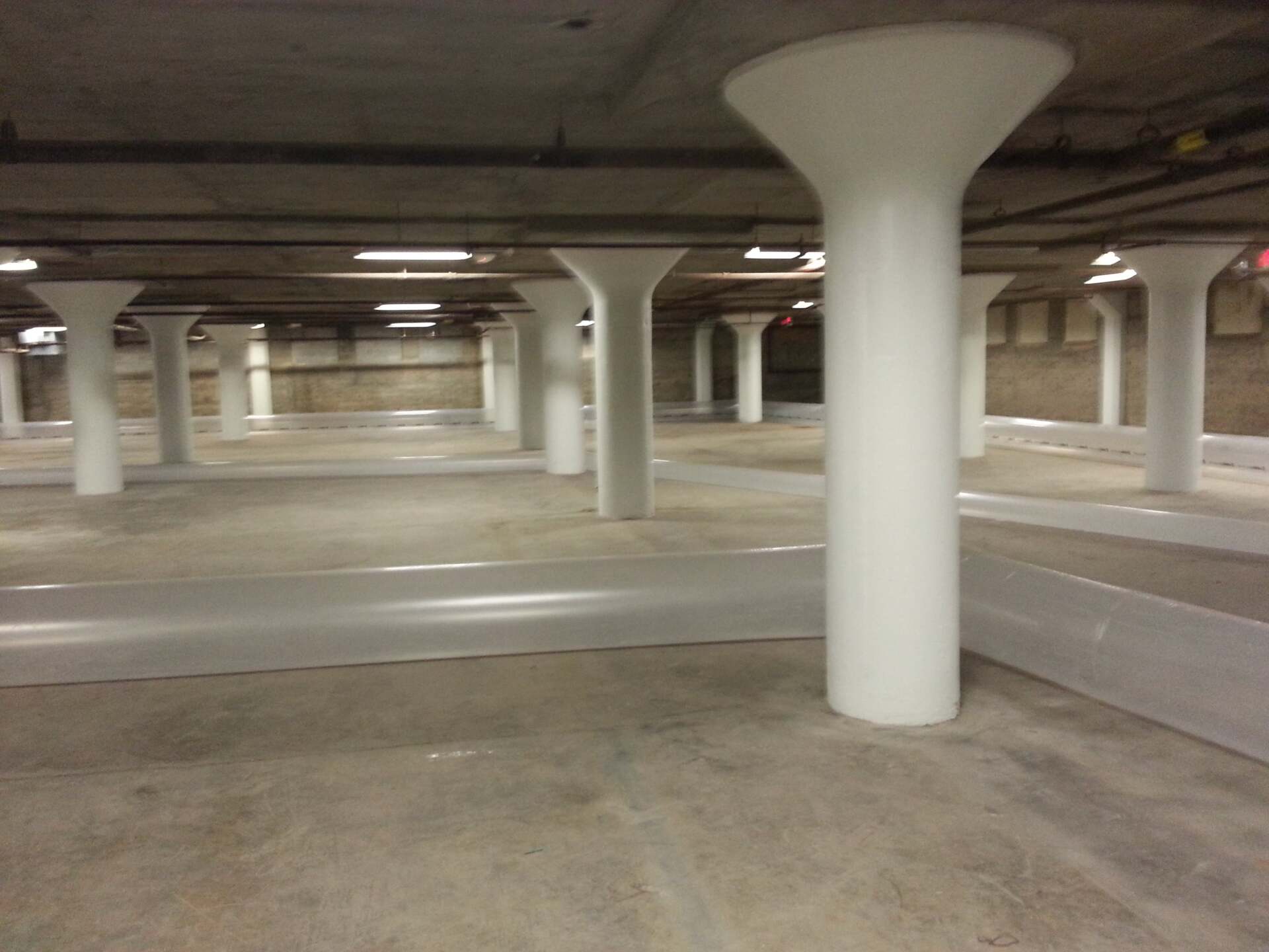 An empty parking garage with white columns and a red exit sign