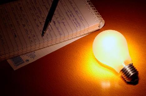 Glowing light bulb next to a notepad 