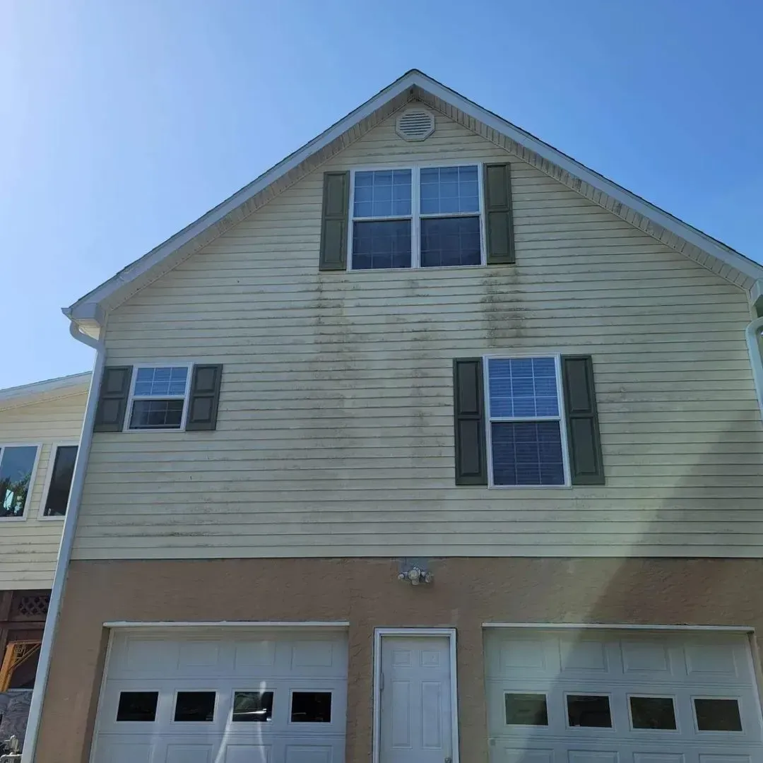 Two-story house with tan siding, two garage doors, and green shutters.