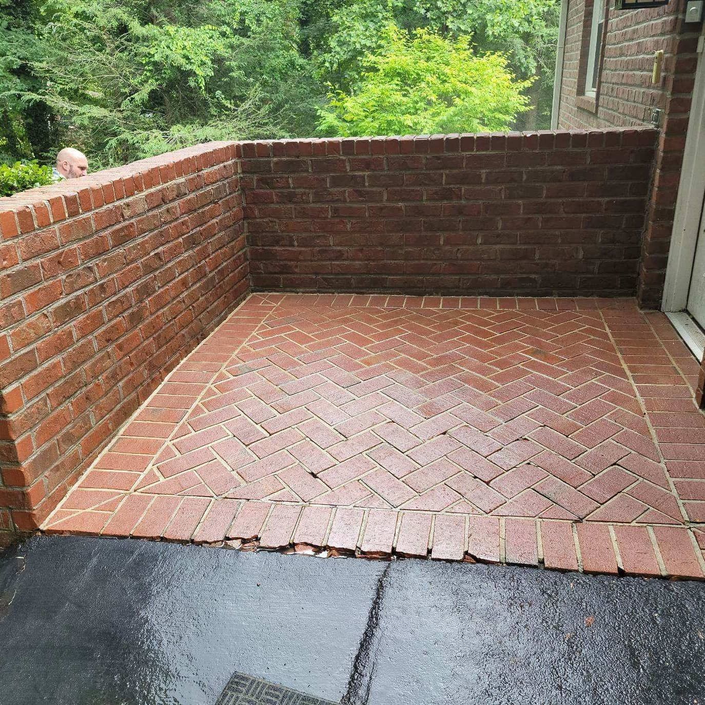 Brick patio with herringbone pattern, surrounded by brick walls and a tree backdrop.