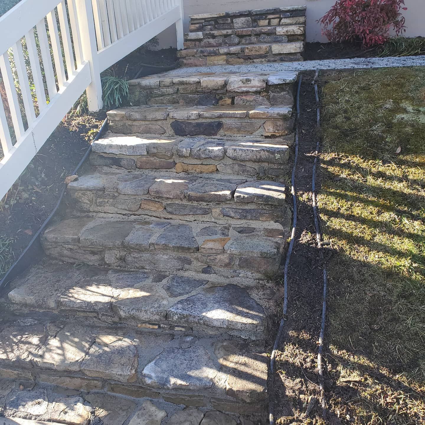 Stone steps leading up to a house with a white railing. Grass and mulch border the steps.