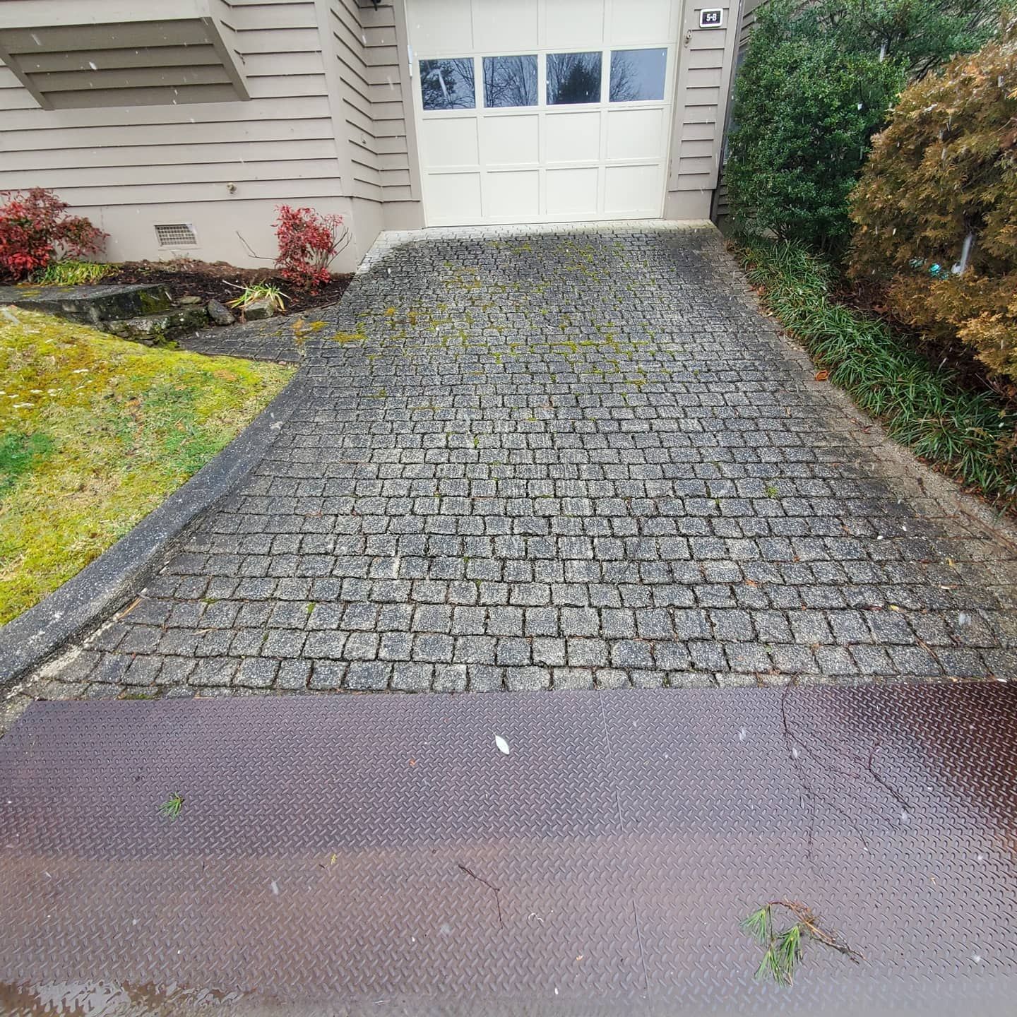 Driveway paved with cobblestones leading to a garage door. Green plants border the sides.