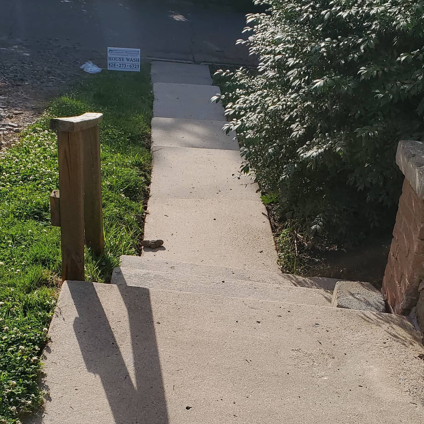 Concrete steps leading up to a building, with a wooden handrail on the left.