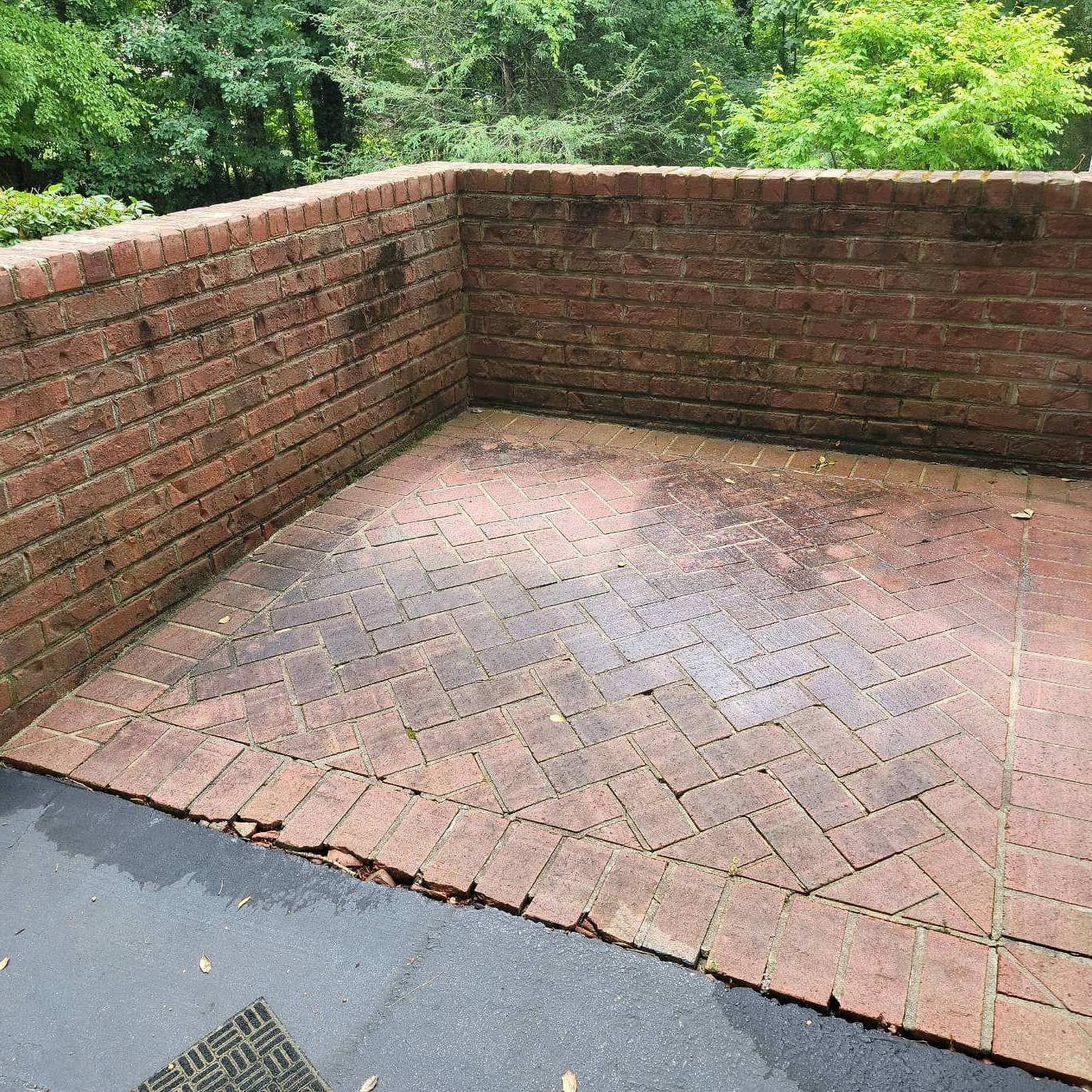 Brick patio enclosed by brick walls, wet with dark stains. Lush greenery in background.