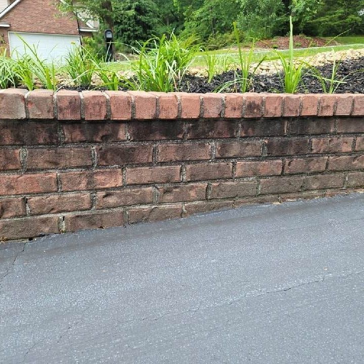 Brick retaining wall with plants on top, next to asphalt driveway.