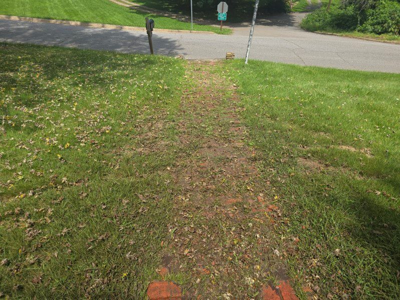 A grassy pathway worn through a lawn leads to a street and road sign.