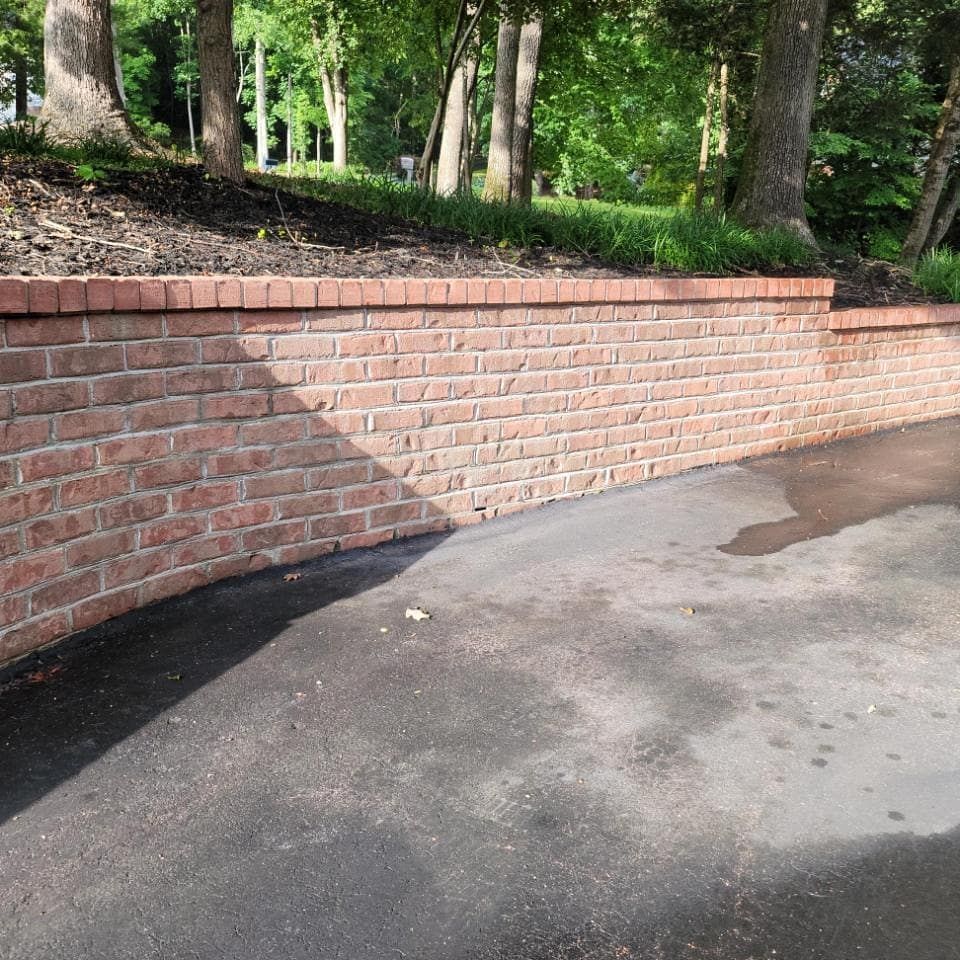 Brick retaining wall curves along a paved driveway, with trees in the background.