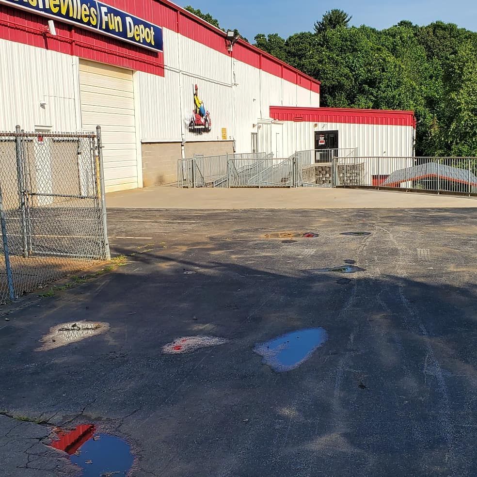 Exterior of Stoneville's Fun Depot with a gray parking lot and a red and white building under a sunny sky.