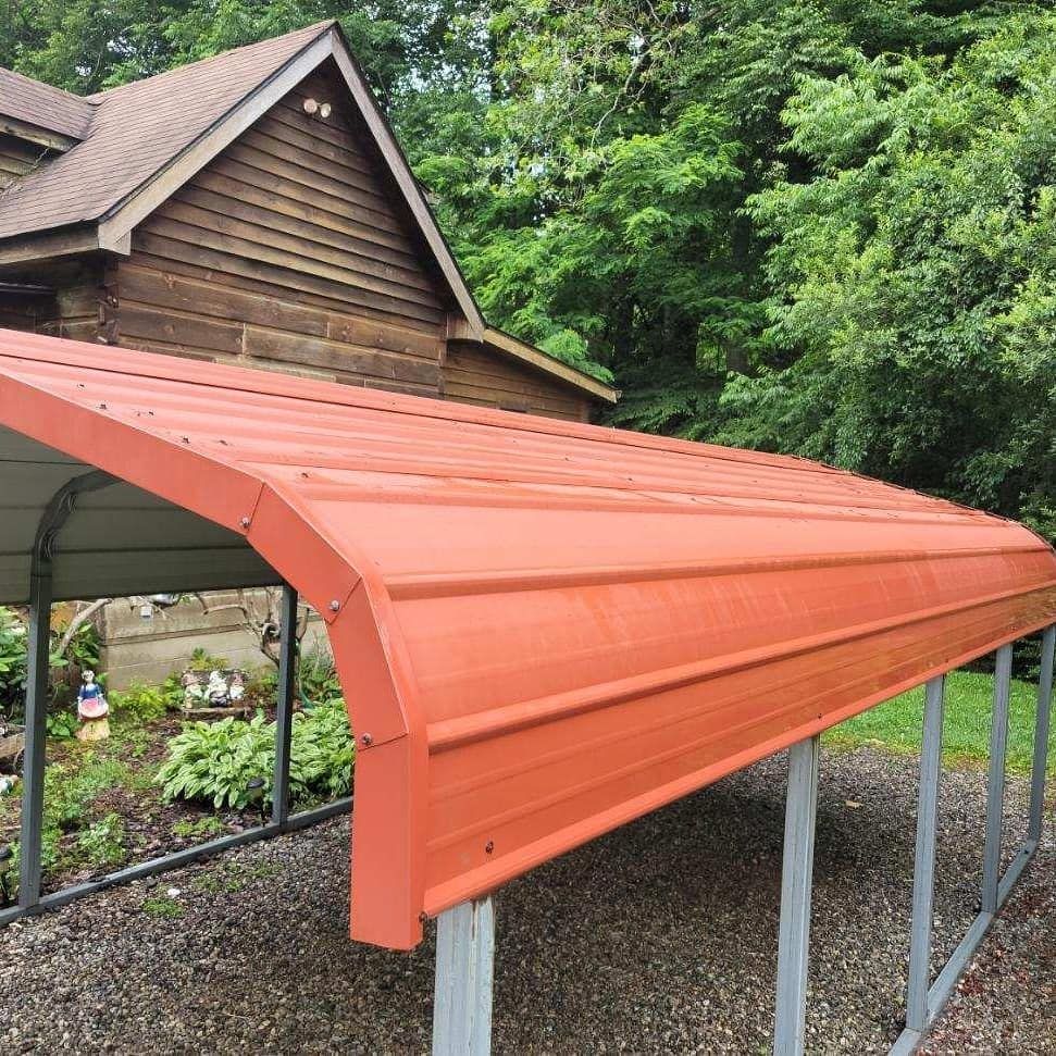 Orange metal carport attached to a brown house with a gravel surface and green foliage.