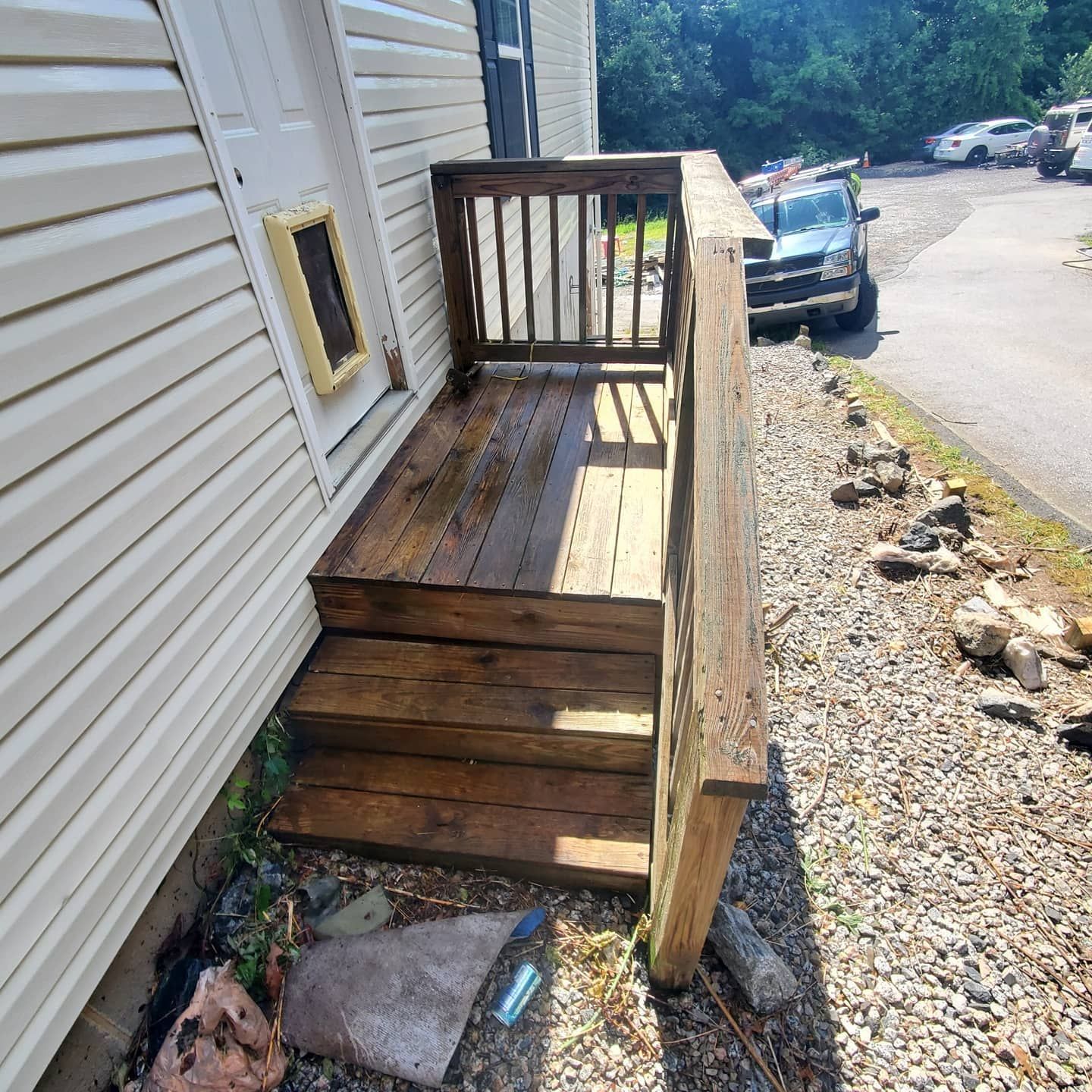 Wooden steps and landing outside a building, with a door and railing.