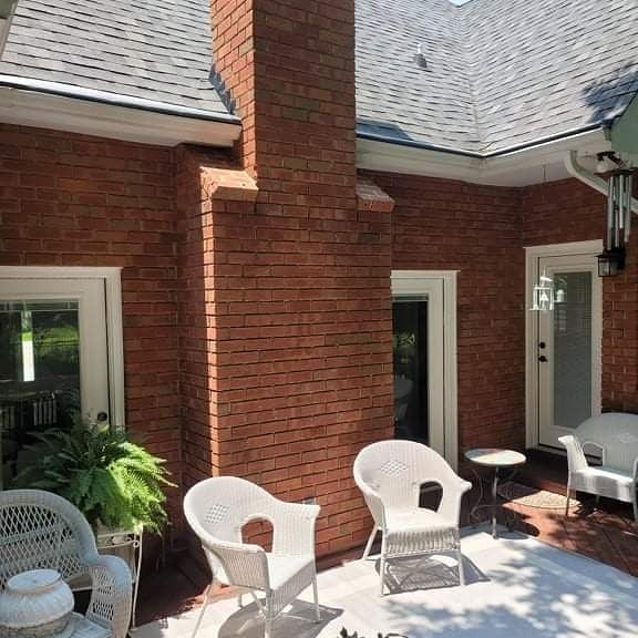 Brick exterior with white wicker furniture on a patio beneath a chimney and roof.