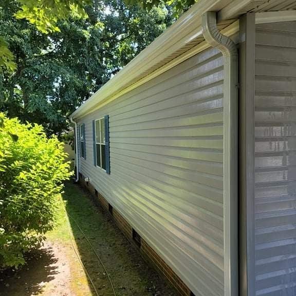 Side view of a light gray house with matching gutters, green bushes, and a blue shutter.