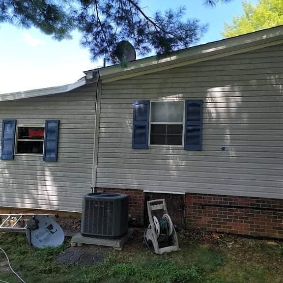 Side of a light gray house with blue shutters, satellite dish, and AC unit.