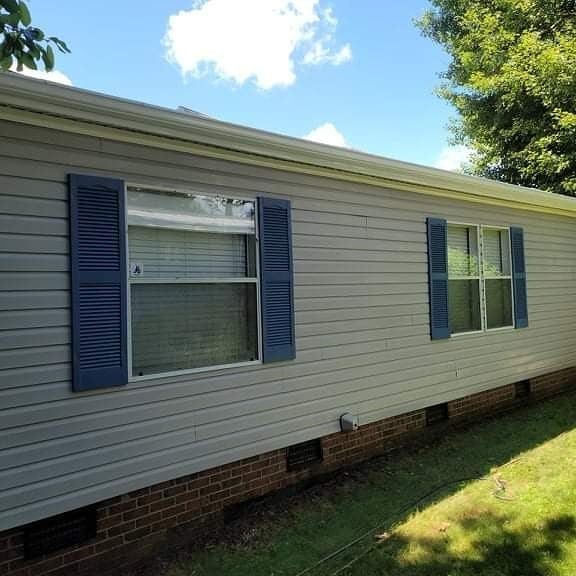 Light gray house siding with blue shutters and a brick foundation.