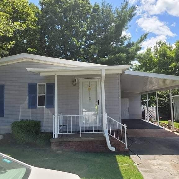 Light gray house with carport, white railing, blue shutters, and a lawn.