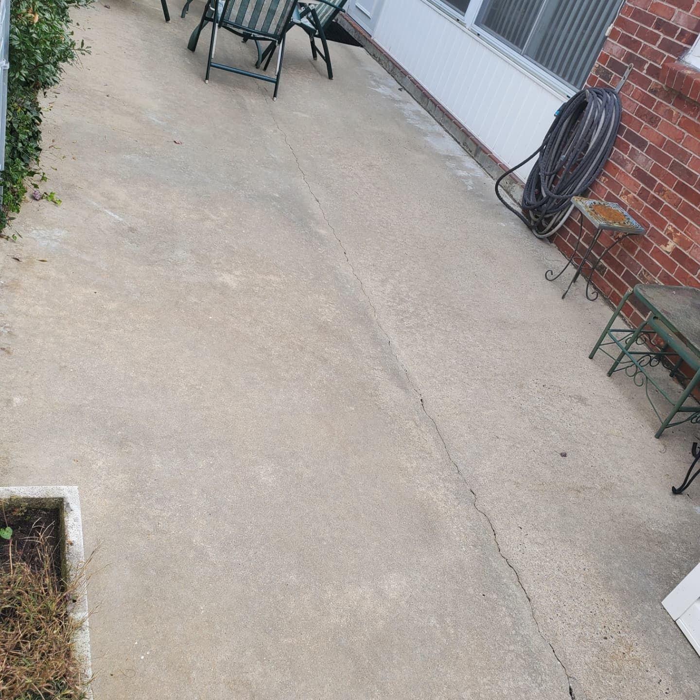 Concrete patio with cracks, chairs, hose, and brick wall.
