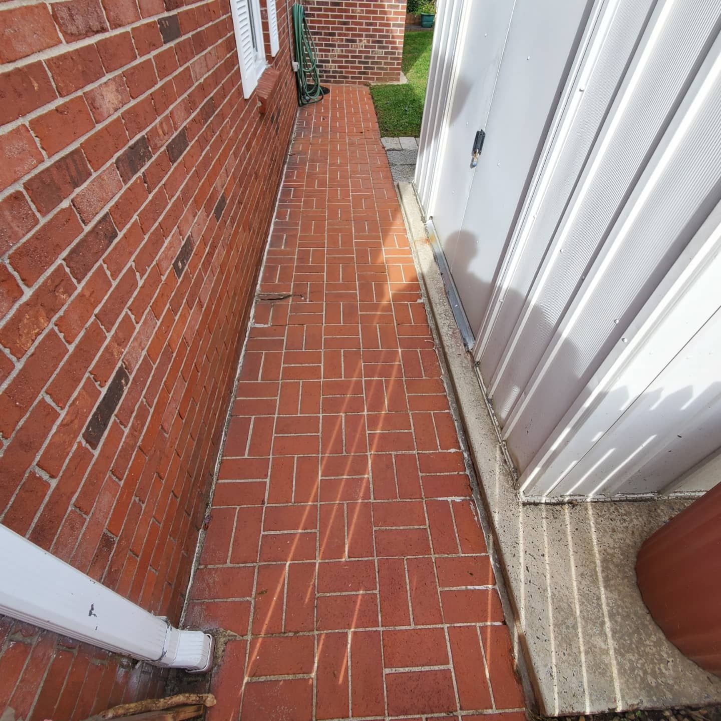 Brick pathway between brick wall and white shed.