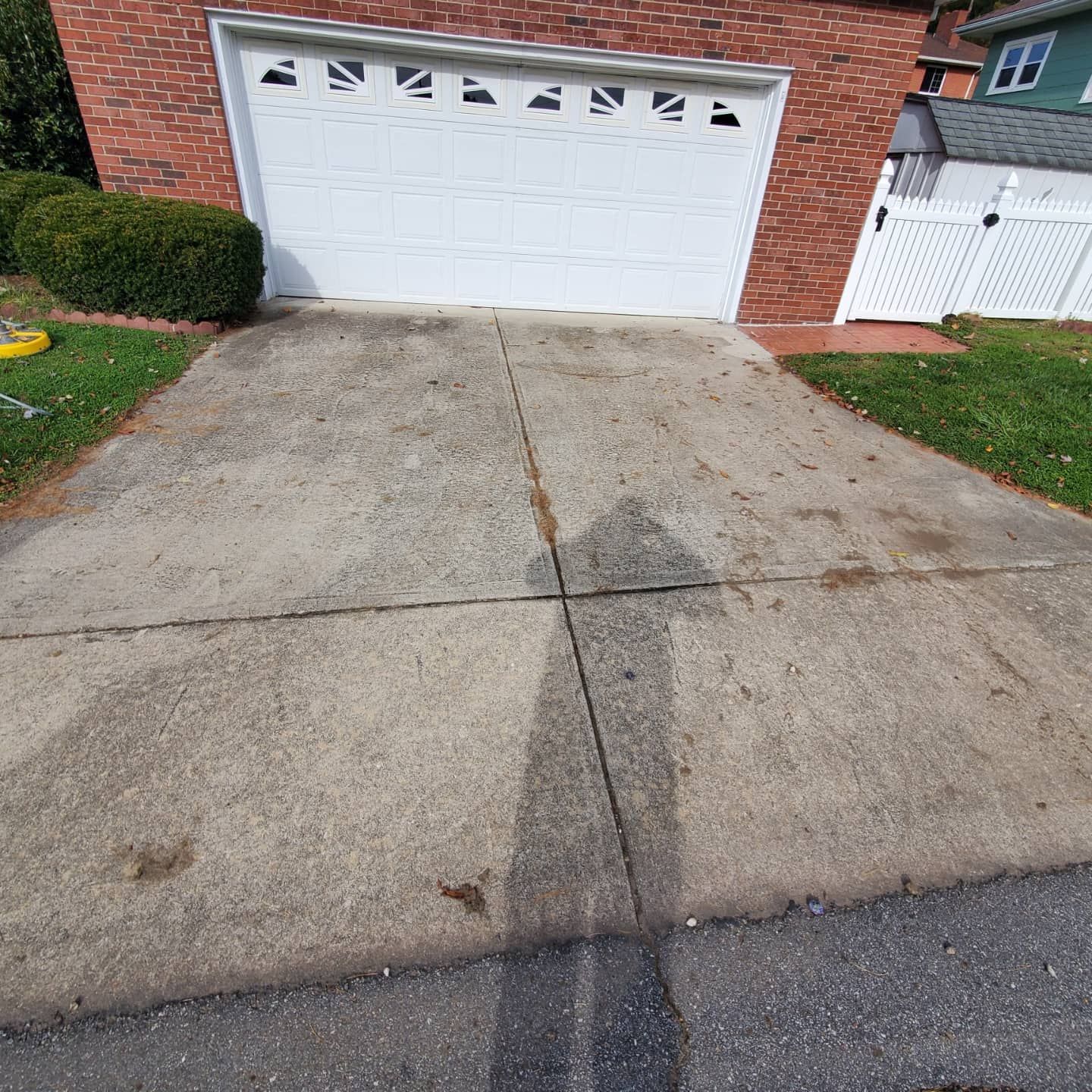 Concrete driveway leading to a white garage door, surrounded by grass and a brick house.
