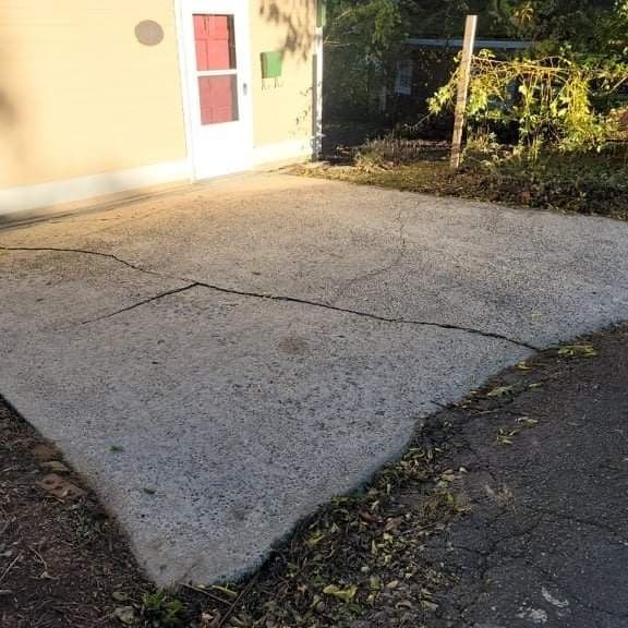 Cracked concrete driveway with a white door, a bit of the house, and some leaves.
