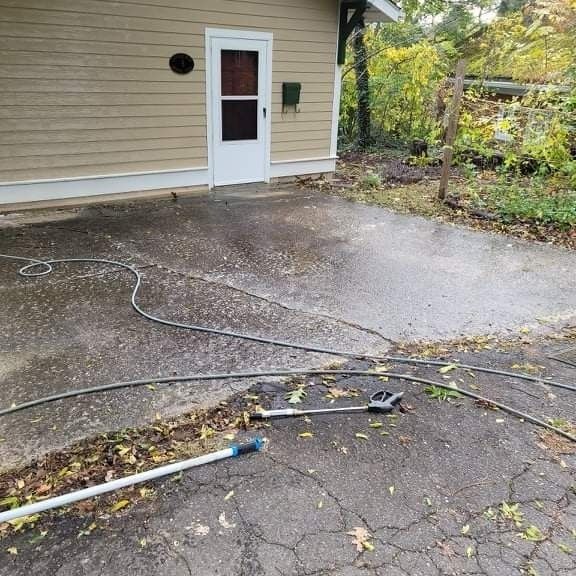 Asphalt driveway being power washed near a tan building with a white door.