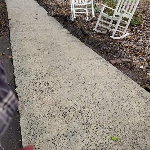 Concrete sidewalk with two white rocking chairs on the right side.
