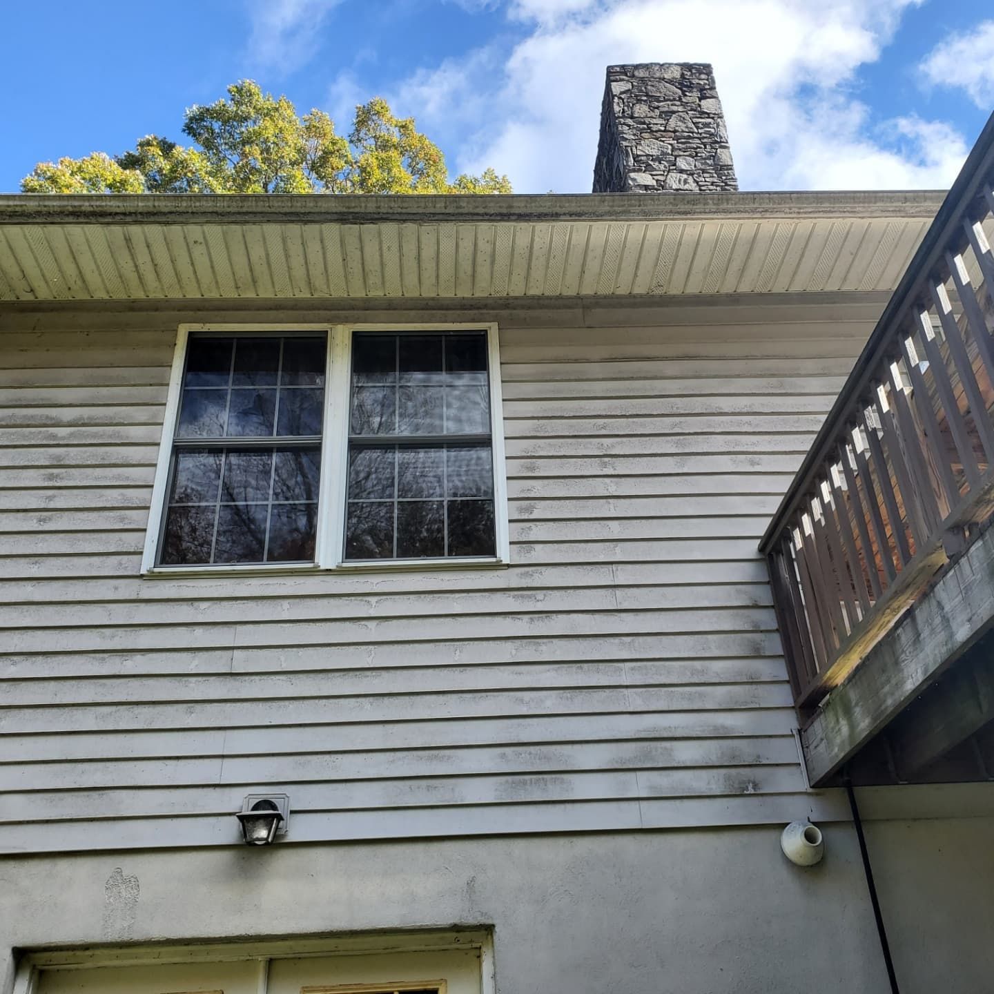 Exterior of a house with two windows, a chimney, and a wooden deck. Cloudy sky.