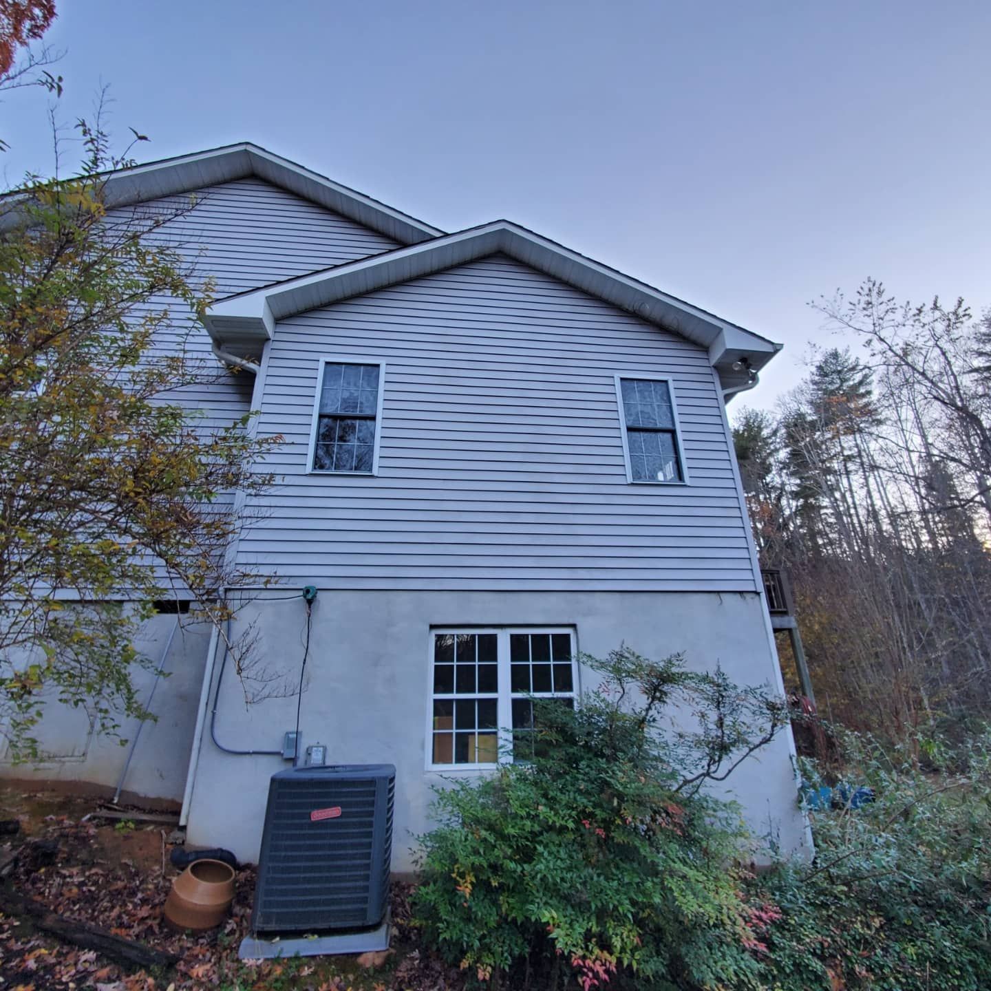 Two-story house with gray siding, two upper windows, one lower window, and an air conditioning unit.