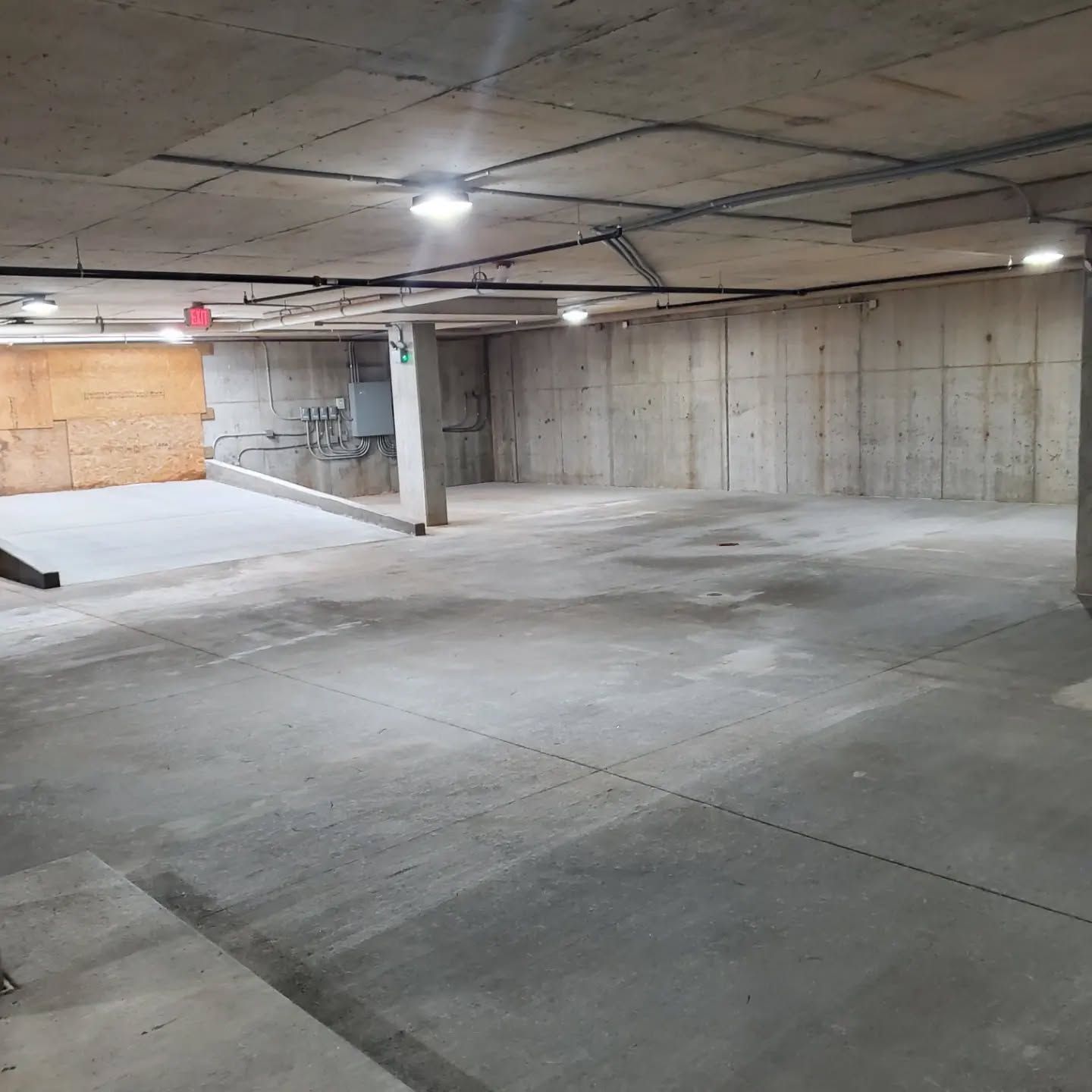 Empty concrete parking garage with ceiling lights and conduit.