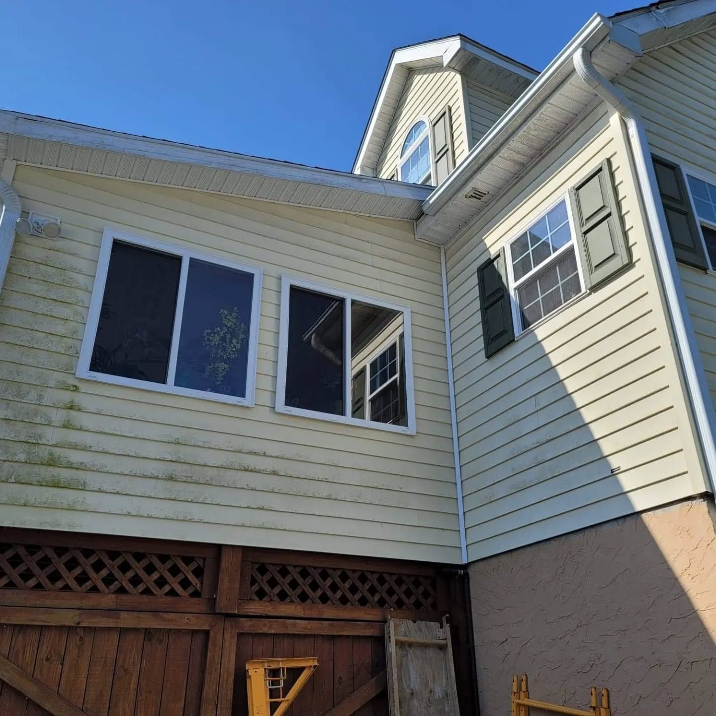 Beige house exterior with windows, green shutters, and a wooden lattice.