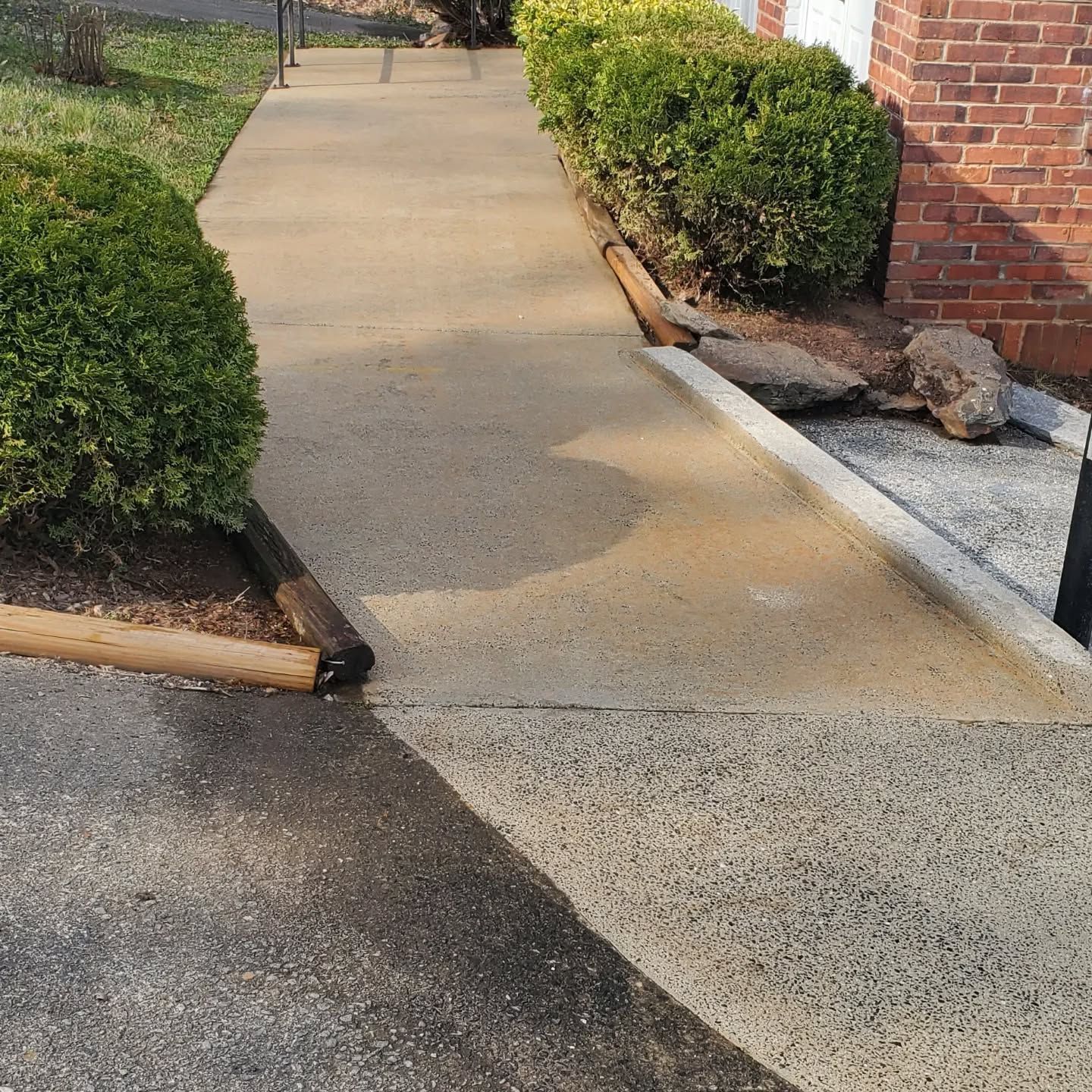 Concrete walkway with bushes on either side; a brick building is on the right.