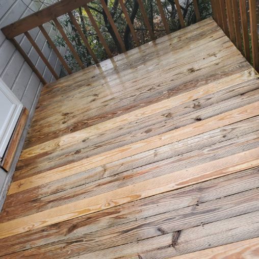 Wooden deck with wet, weathered planks under a covered area, next to a wall.